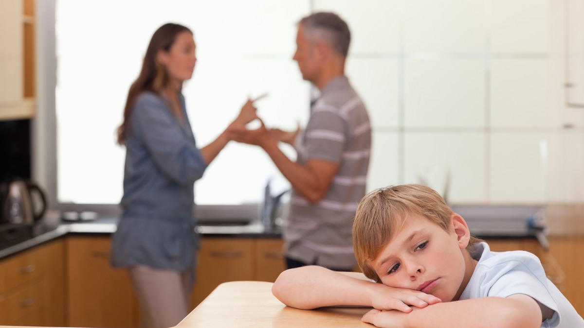 Bild: Ledsen pojke vid matbordet medan hans föräldrar bråkar bakom honom