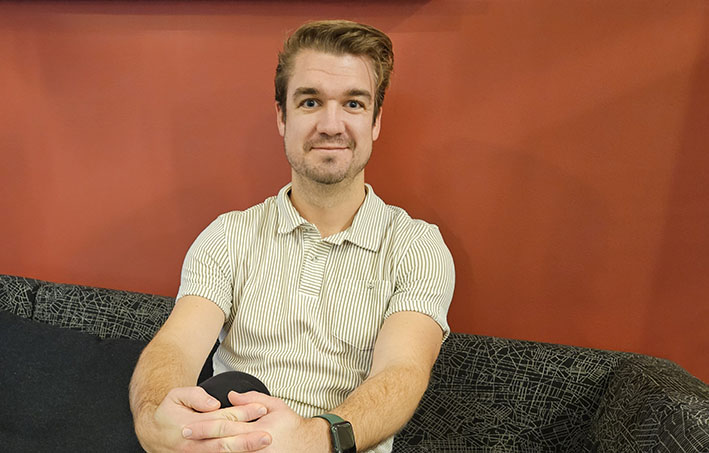 Erik Selander sitter på en svart soffa med benen i kors.